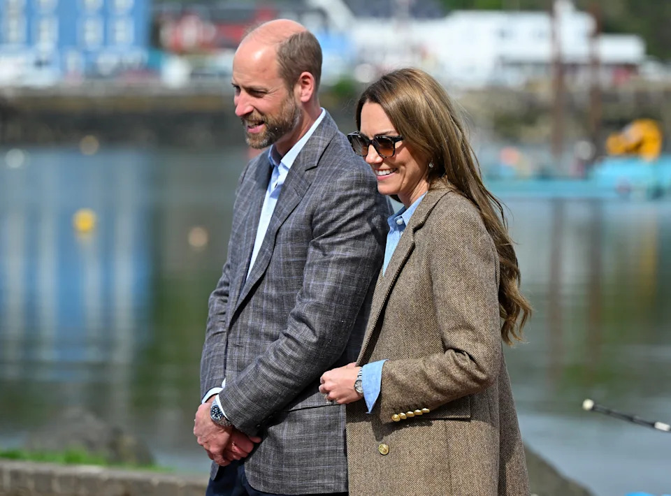 Prince William and Princess Kate smiling in front of a waterfront town