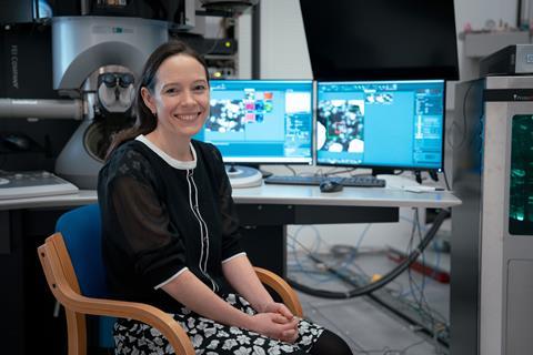 Sarah Haigh sitting at a desk with two computer screens and an electron microscope