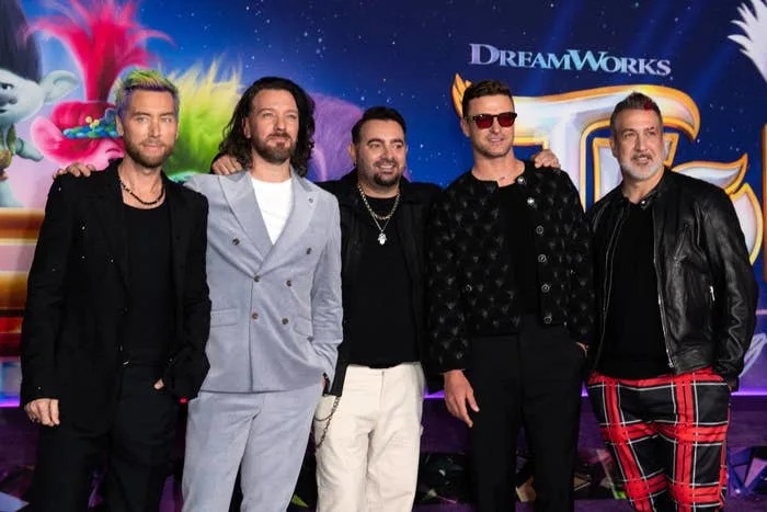 Five people pose together at a DreamWorks event. They wear stylish outfits: casual, suits, and bold patterned pants