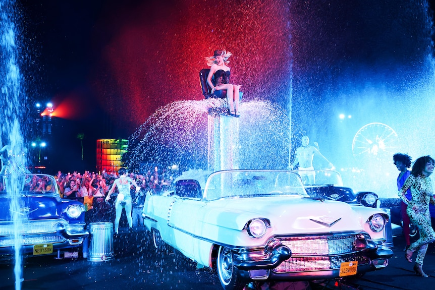 Sabrina Carpenter atop a classic car amid cascading water, dancers, and bright stage lights at Coachella