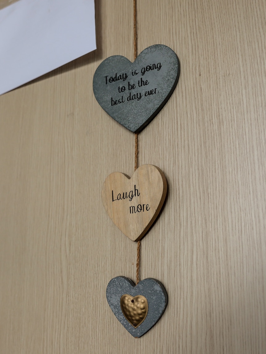 A decoration hangs on a wall it has three hearts hanging on a ribbon. Heart text reads 'Today is going to be the best day ever' 