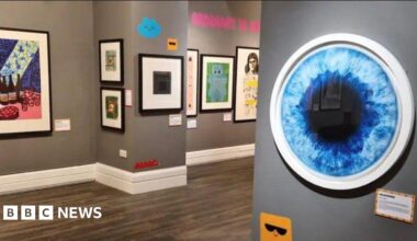 A gallery space with grey walls that has colourful artworks hanging on the walls.