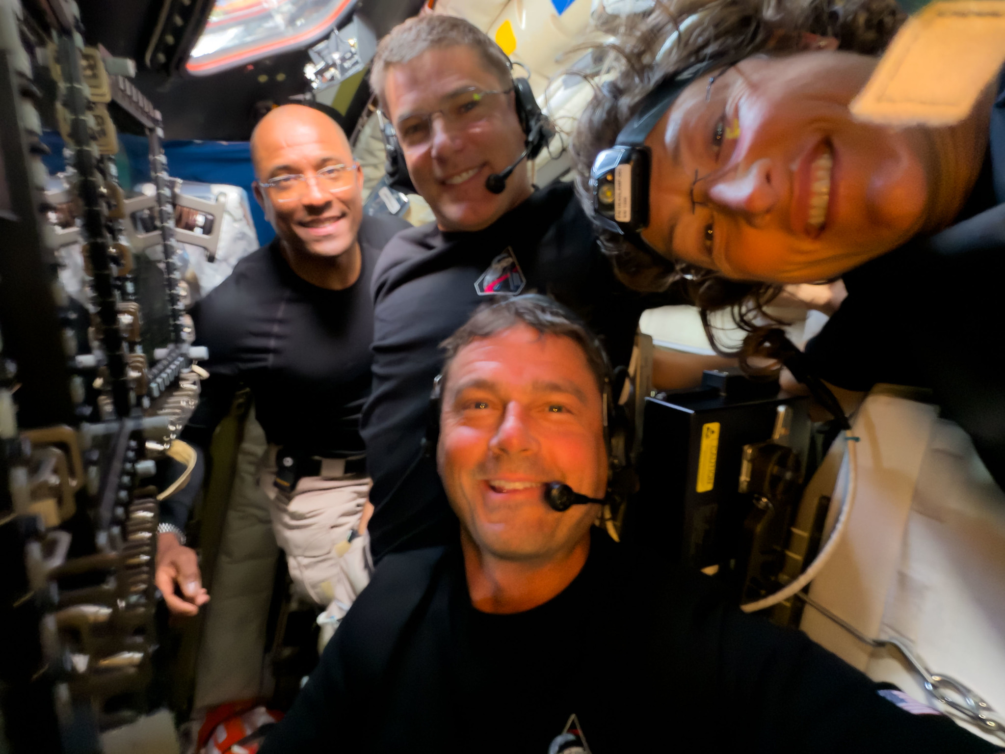 A selfie of four people in a space capsule.