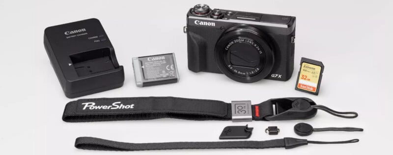 A Canon PowerShot G7 X Mark III camera with accessories, including a battery, charger, 32GB SD card, wrist strap, and small camera parts, all arranged on a white surface.