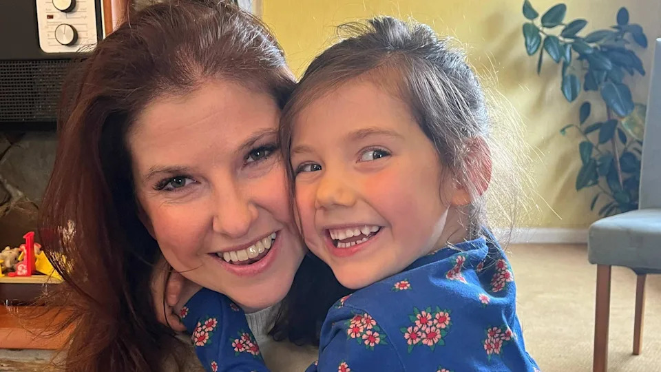 Katy and Molly, both with dark brown straight hair, embrace and smile.