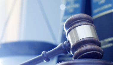 A gavel rests on its sounding block with a several law books and a justice scale out of fucus in the background. A cool blue cast dominates the scene. (A gavel rests on its sounding block with a several law books and a justice scale out of fucus in t