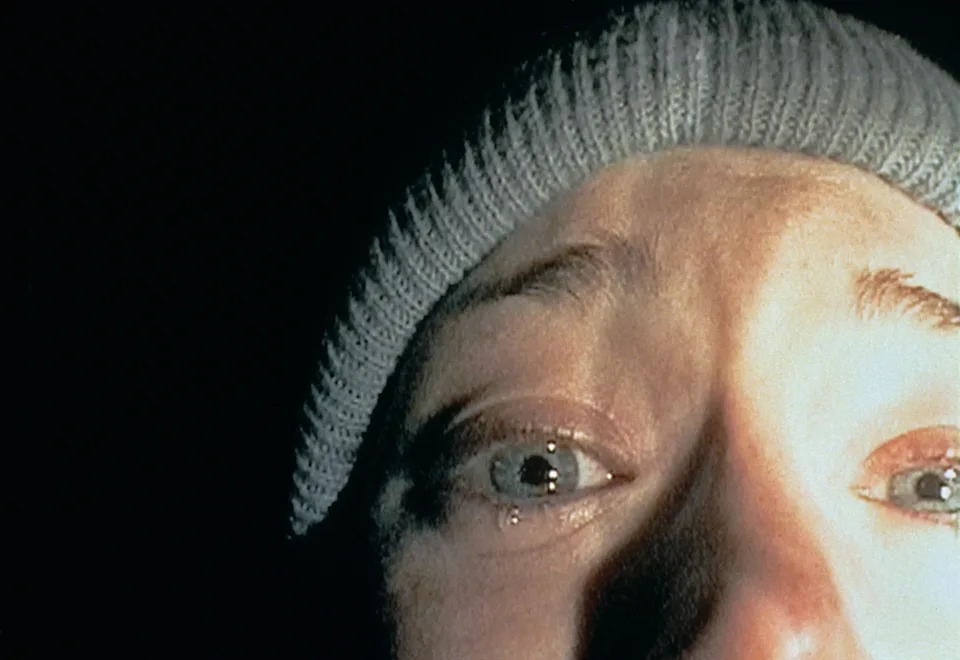 Close-up of a person wearing a knit beanie, looking frightened with teary eyes, in dim lighting