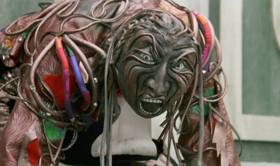 A person in an elaborate, fantasy-inspired costume with textured features, wide eyes, and open mouth, creating an intense and dramatic expression