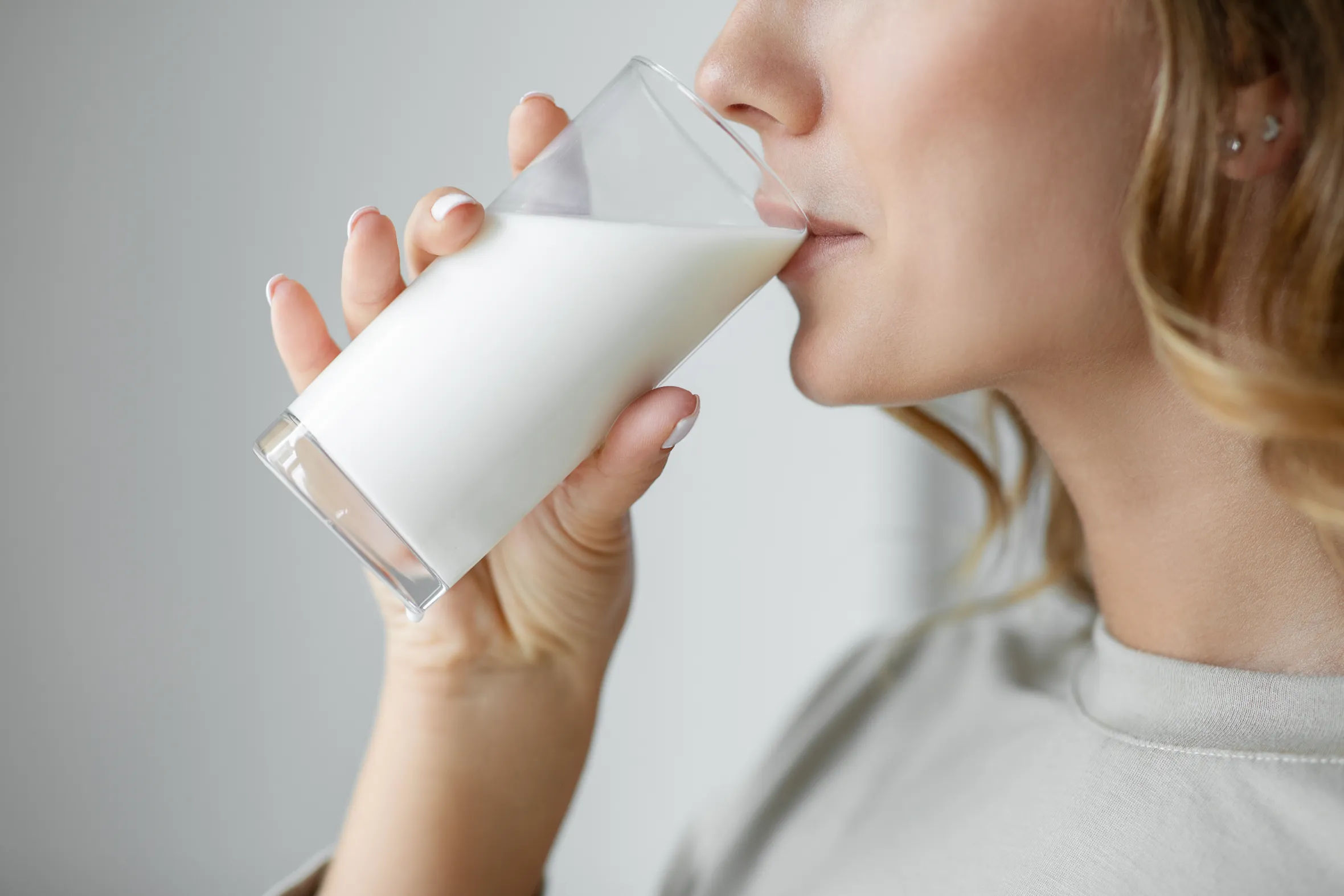 A woman drinking a glass of milk, seen from her left side.