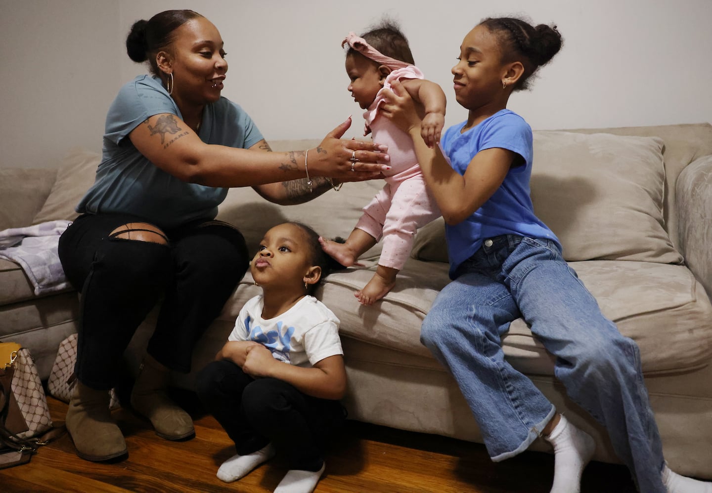 Brianna Smith-Thomson, a 35-year-old mother of three, reached out as her daughter Kennedy, 10, passed her sister 5-month-old Serenity back to her mom as Heavyn, 4, watched television in the family’s living room in Lynn.