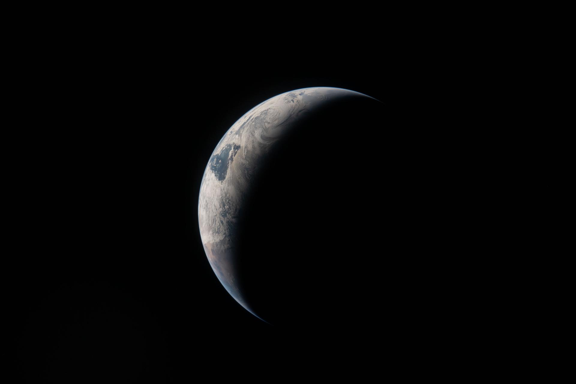 A photo from Artemis II A thin arc glowing in the darkness of space. Sunlight traces the curves of the ocean and clouds, while the rest of the planet fades into shadow.