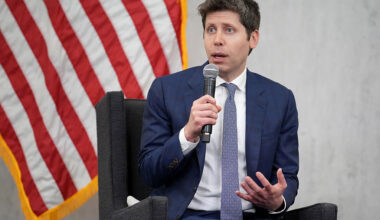 Sam Altman, CEO of OpenAI, sitting in front of American flag