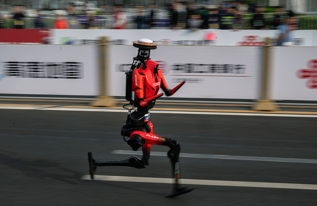 The fastest humanoid robot, an H1made by Honor, runs beside human runners at the start on its way to winning the Beijing Humanoid Half Marathon.