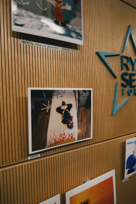 A photo on a wooden wall shows a child dressed as Spider-Man lying on a bed with spiderweb and flame decorations. The label "ENZO" is below the photo, and another label reads "MENTAL HEALTH INPATIENT CENTER.