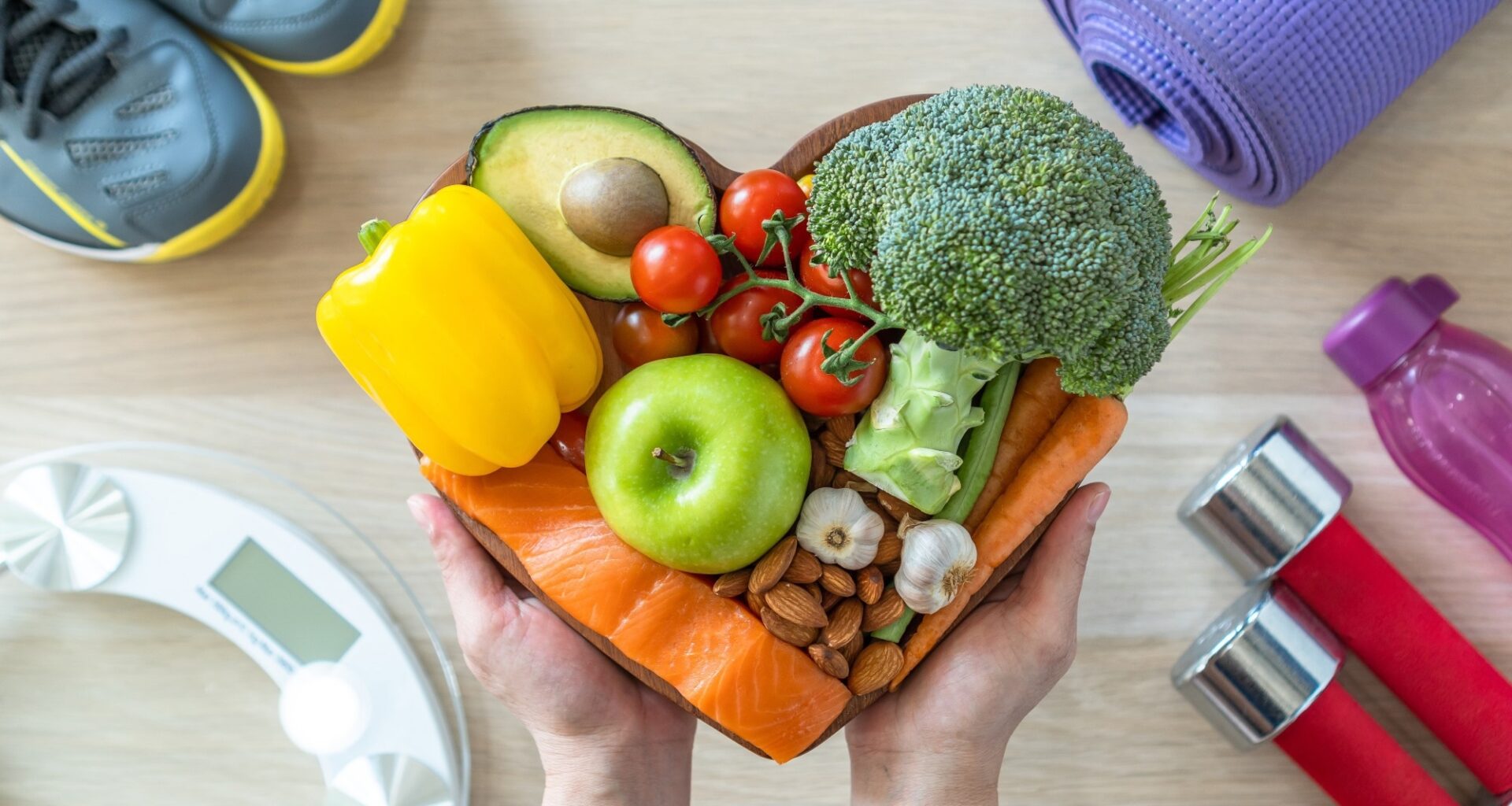 Heart shaped plate filled with vegetables. Background shows running trainers, small dumbbells and scales for heart health and nutrition concept