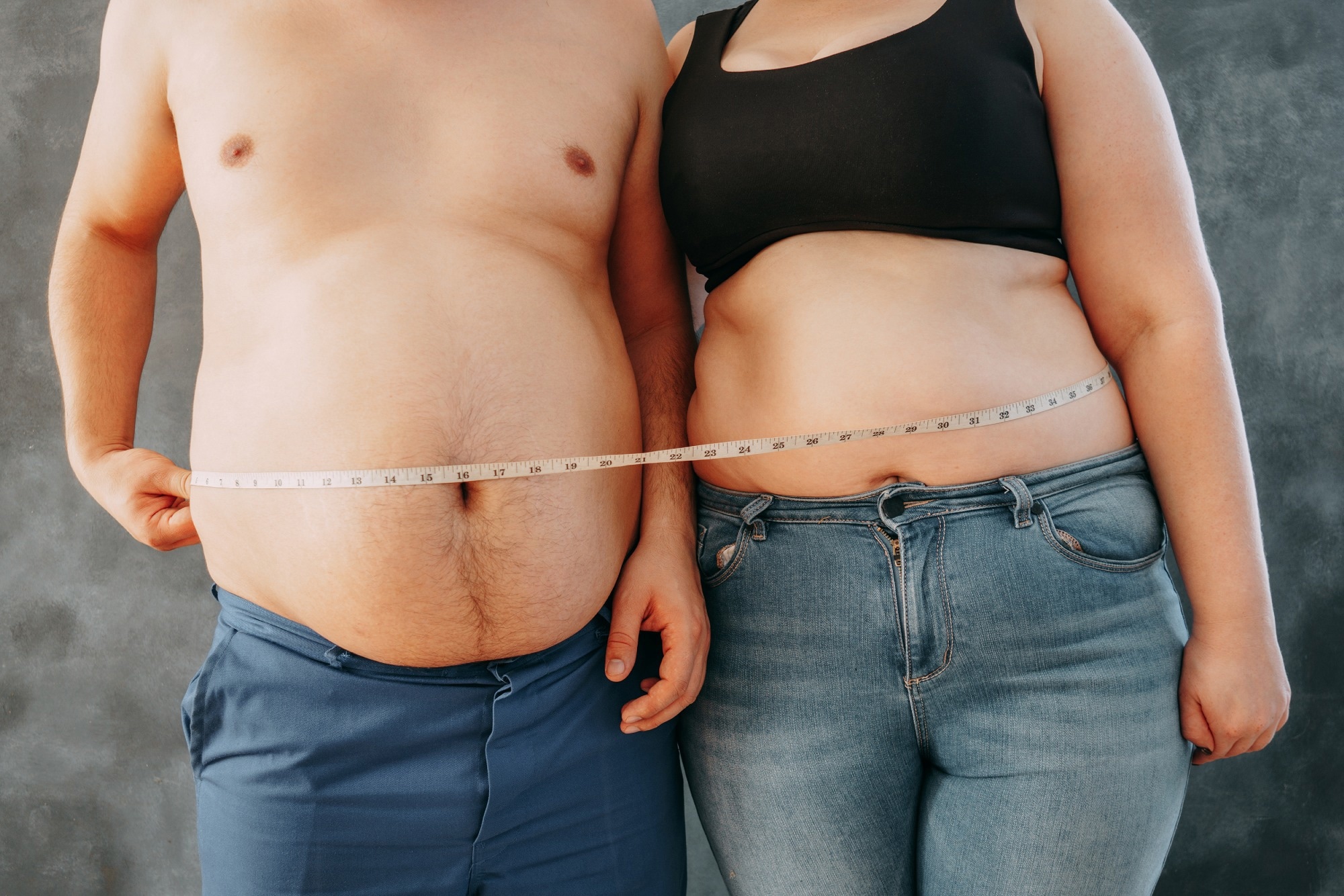 Overweight couple standing together wrapped with measure tape.