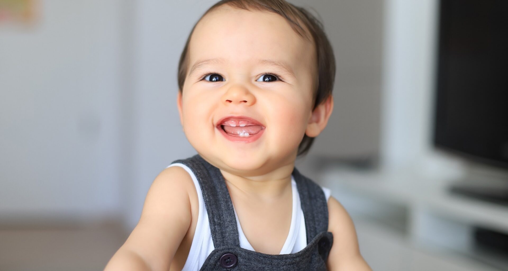 Headshot portrait of cute smiling baby with first milk teeth. Mixed race Asian-German infant laugh and having fun at home. Happy and healthy child about 9-10 months old.