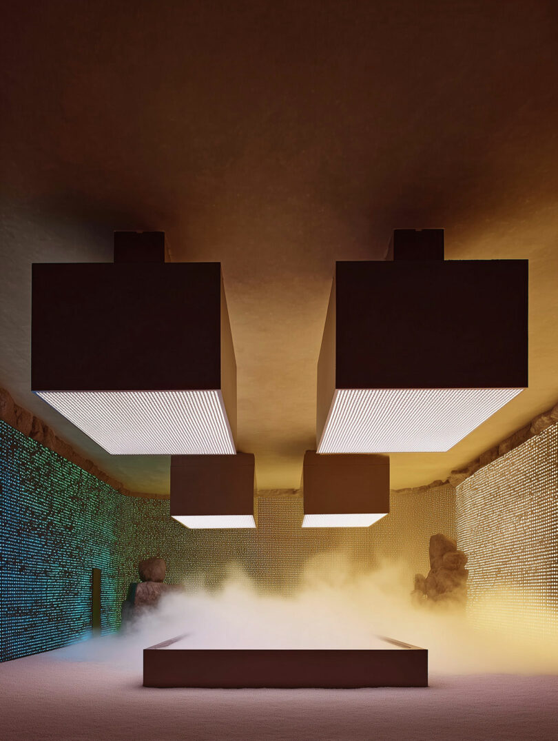 Geometric, glowing rectangular light fixtures hang from a ceiling above a mist-covered platform in a modern, mood-lit room with textured walls.