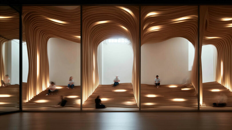 People sit on tiered wooden seating with illuminated, sculptural wave-like designs on the walls in a modern, minimalist interior space.