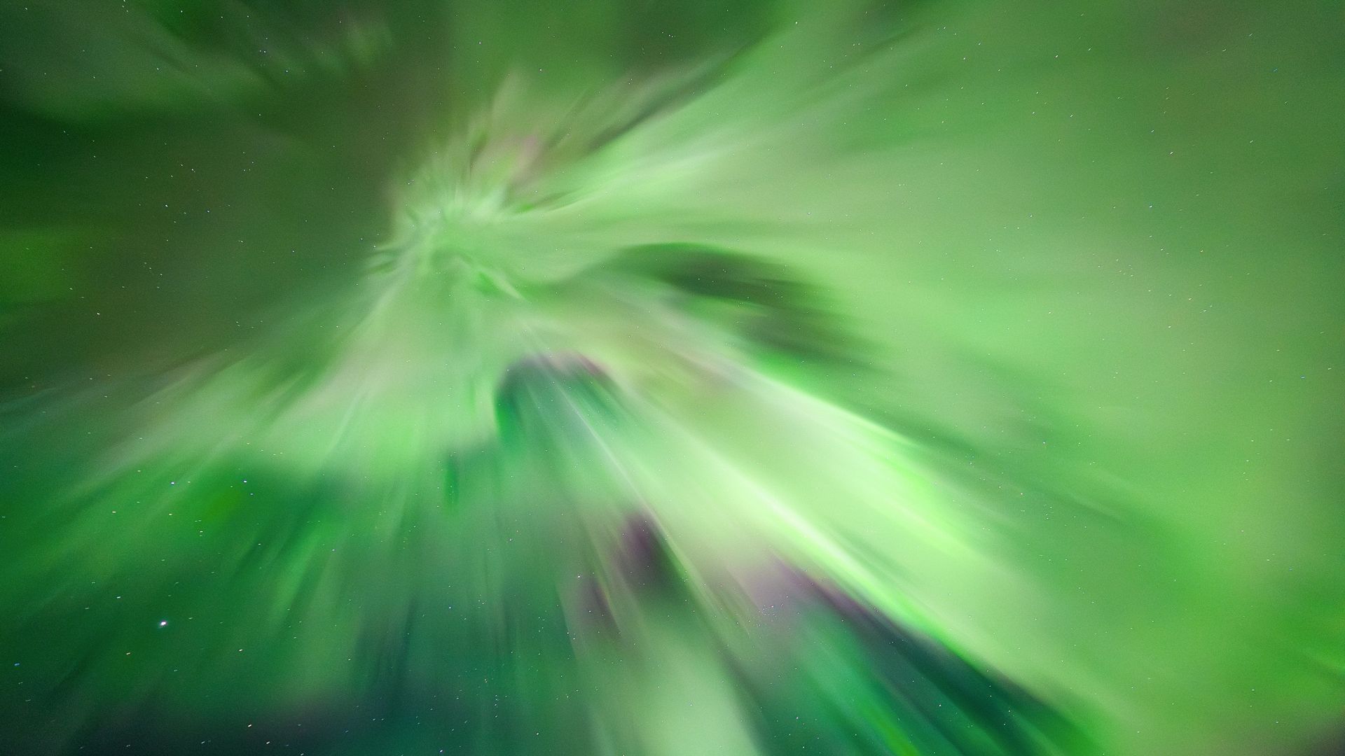 vivid ribbons of green and pink swirl through the deep blue sky.