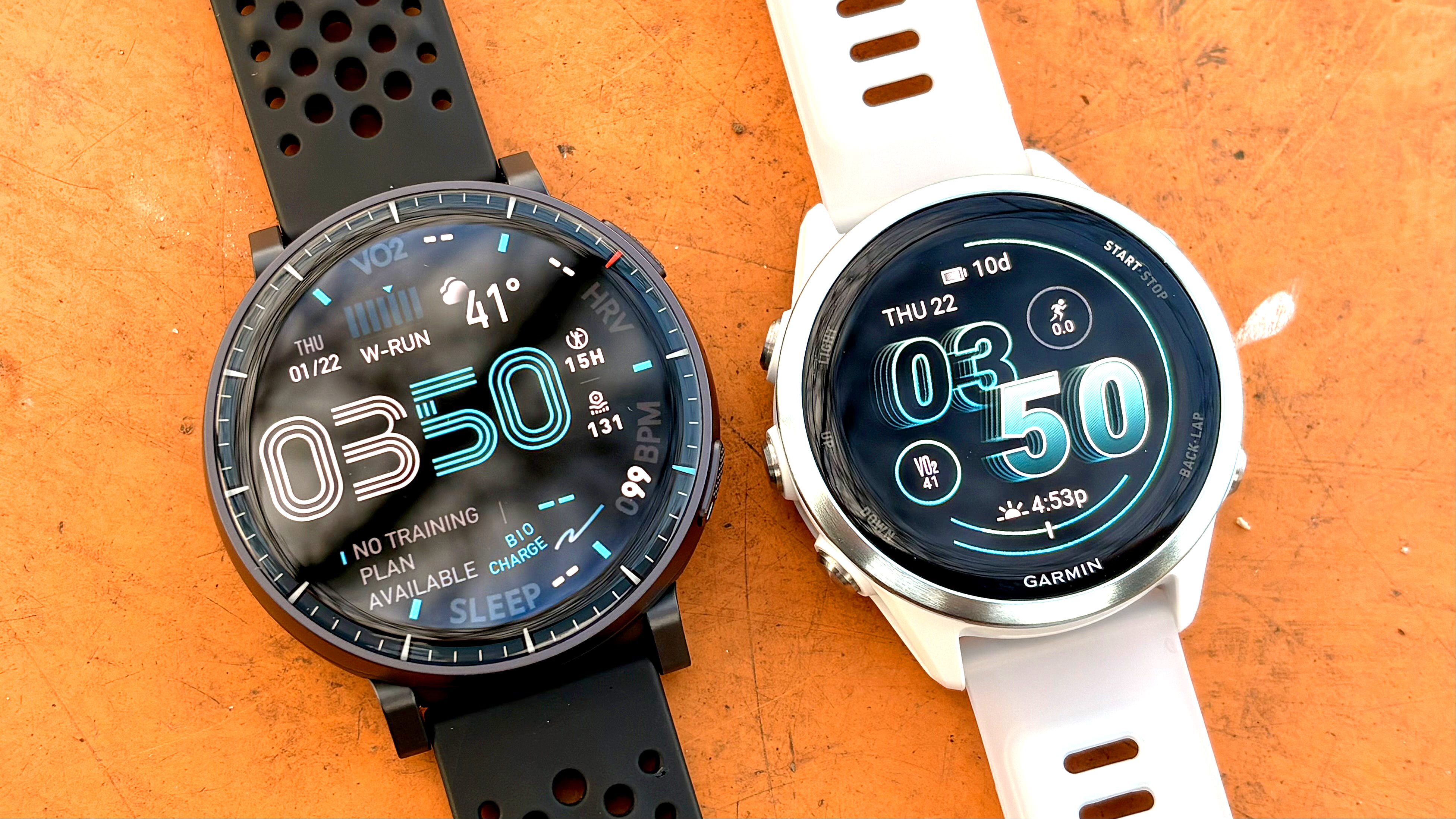 Close-up of the Amazfit Active Max next to the Garmin Forerunner 570 on a bright orange table