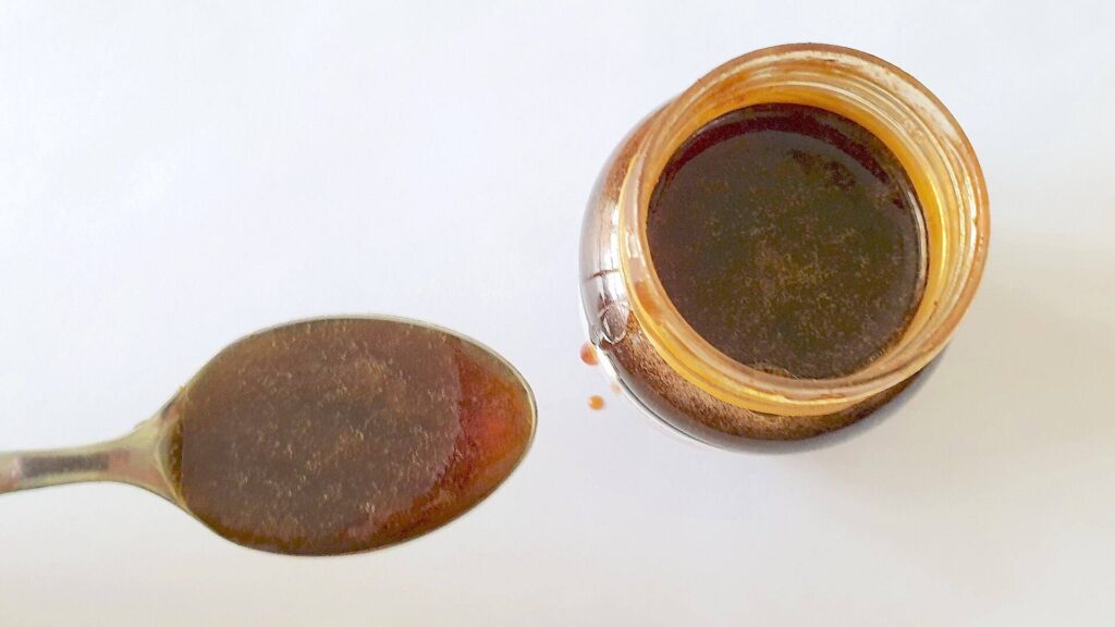 Overhead view of honey in a spoon and in a nearby jar against a white background