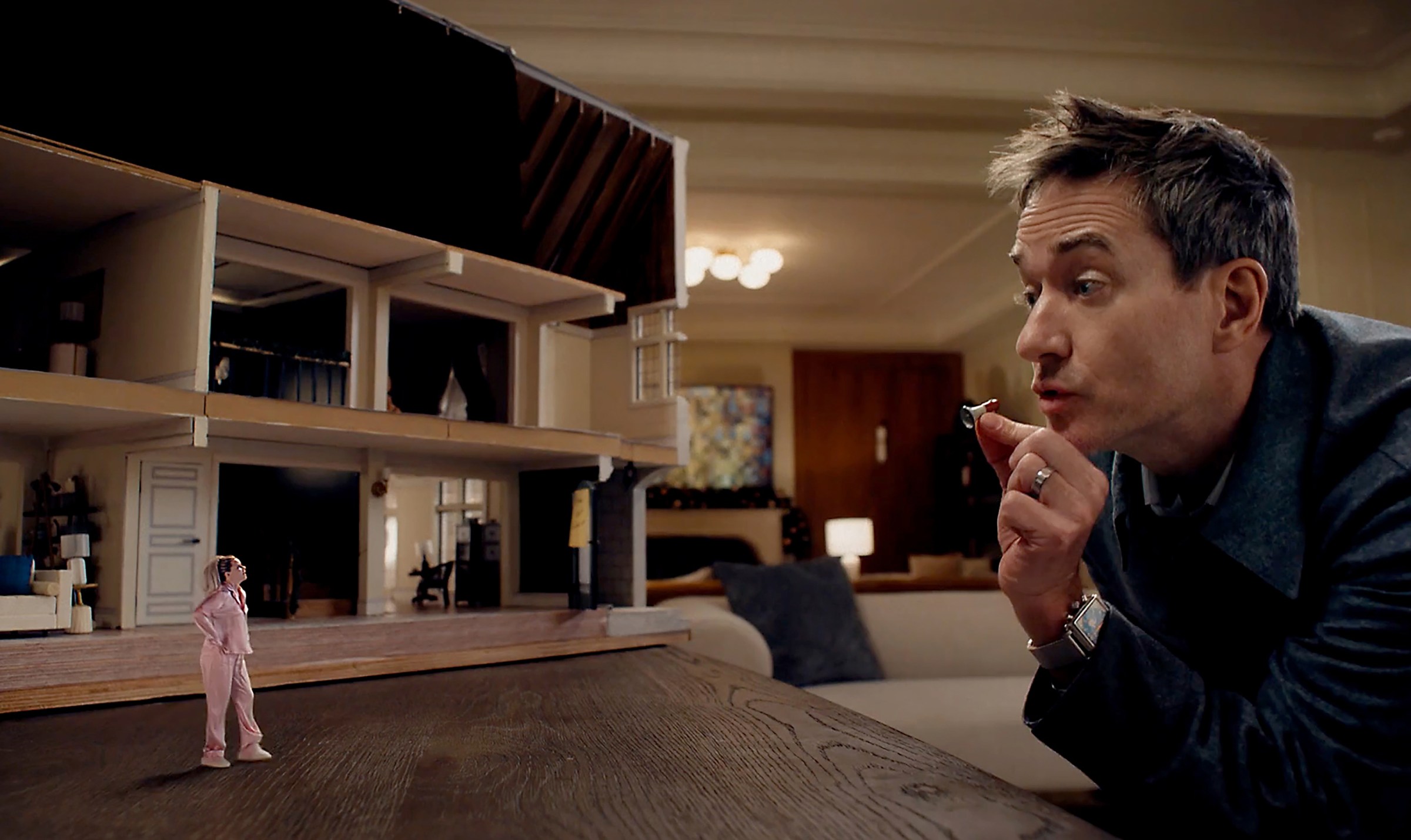 A tiny woman standing next to a bisected dollhouse as she has an argument with a gigantic man the size of a mountain.