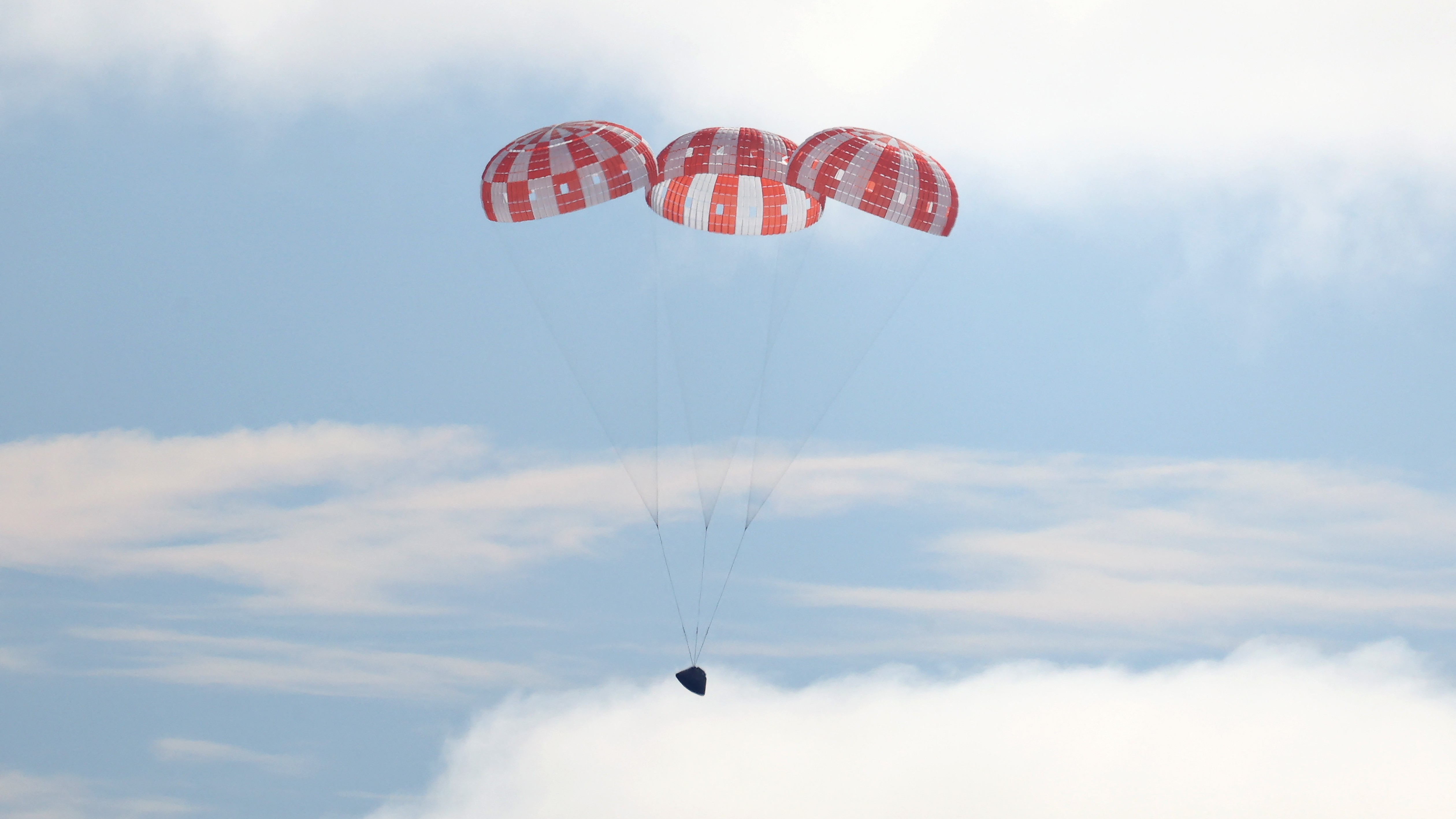 Parachutes deploy behind the falling Artemis I Orion capsule.