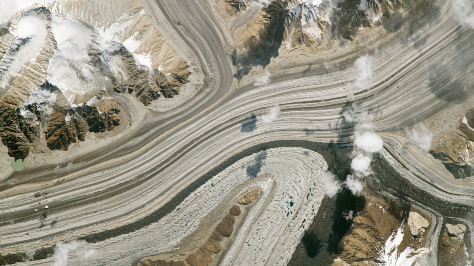 A satellite photo of multiple stripy glaciers merging into a single ice mass