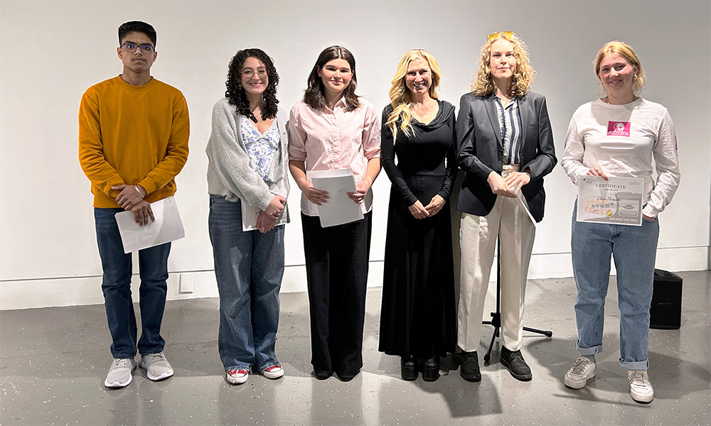 A group of six people stand in a line against a blank wall.