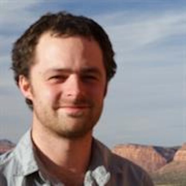 Smiling young man with desert mesas and a canyon in the distance behind him.
