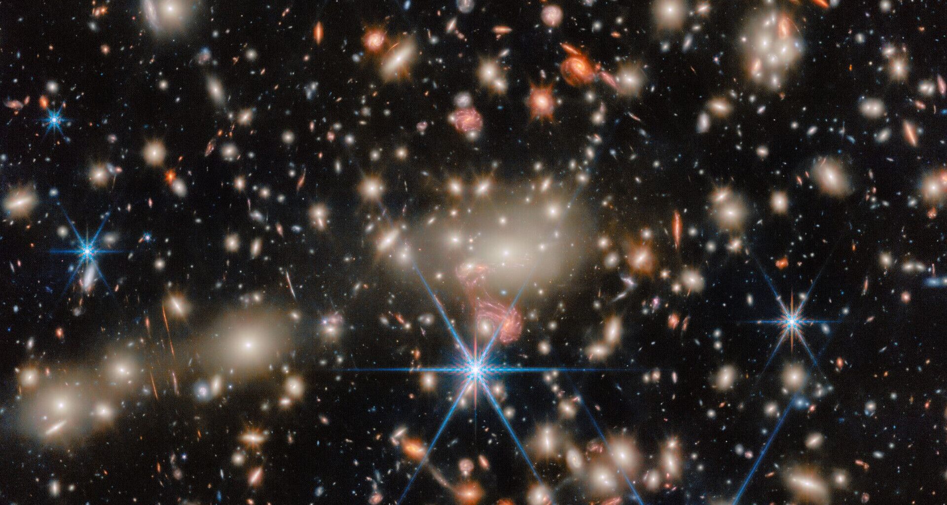 An image of deep space, where blue, red and orange stars twinkle next to golden and orange galaxies.