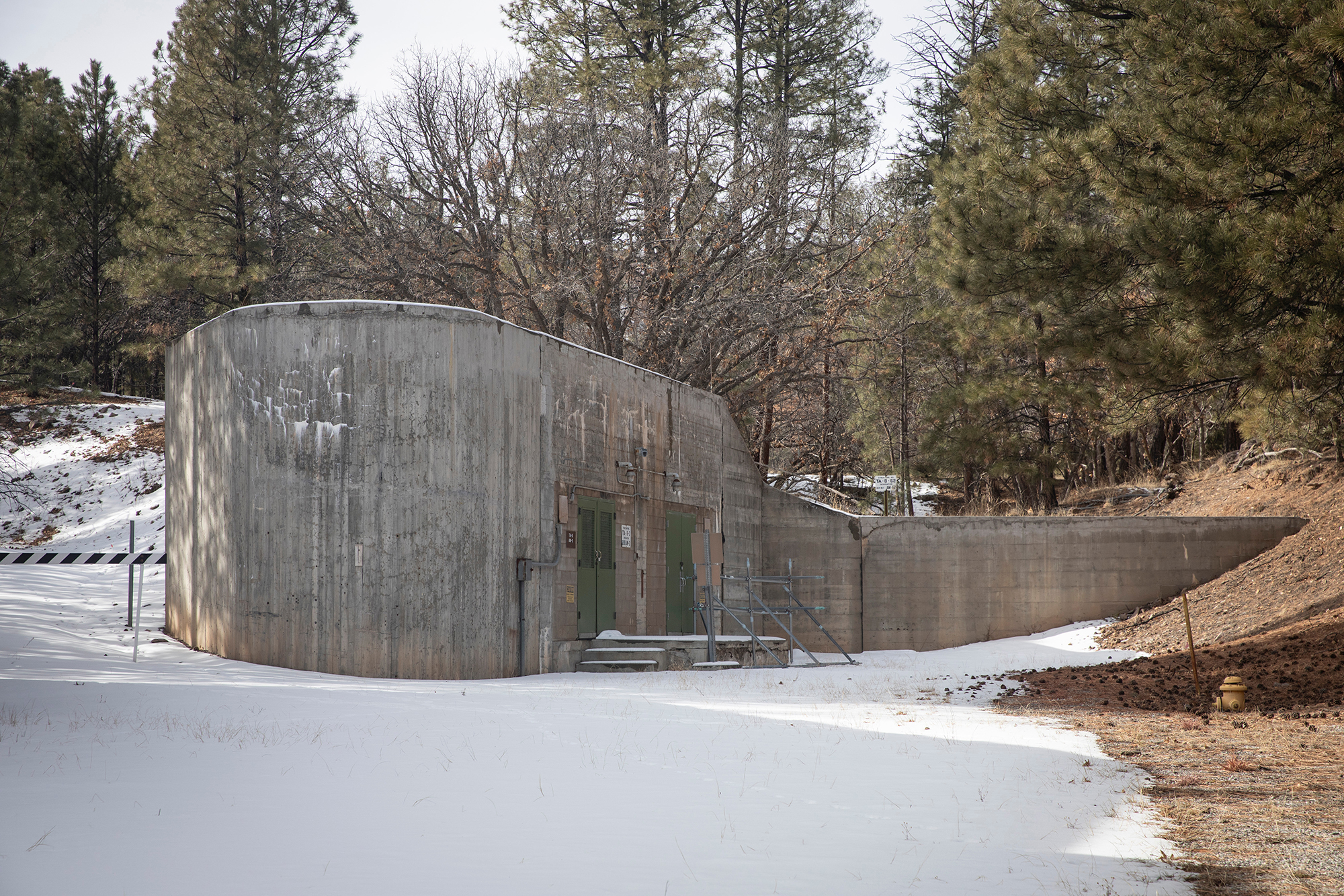 the snowy exterior of a windowless, concrete building backed up to forest