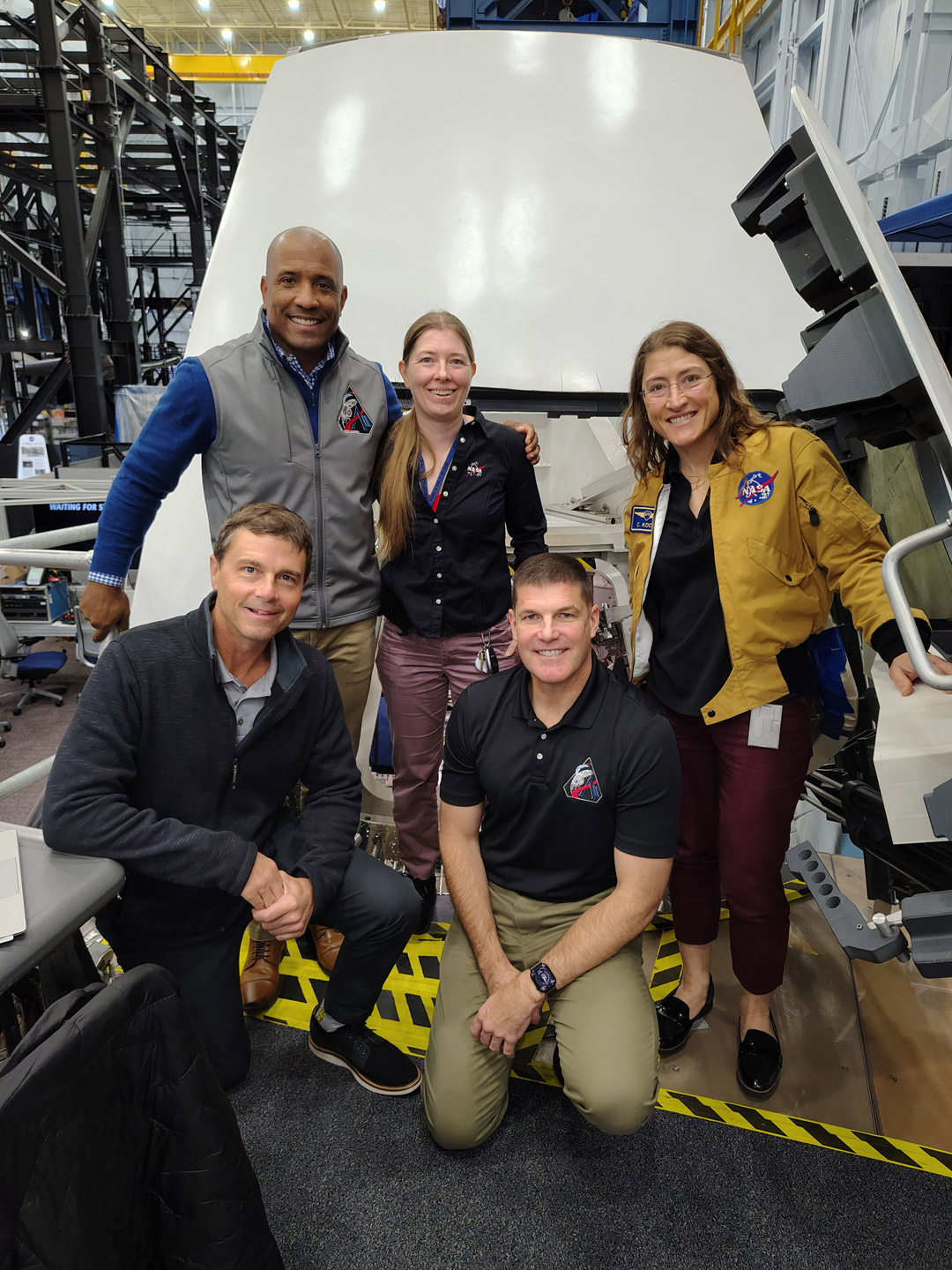 Five NASA team members pose beside spacecraft simulator.