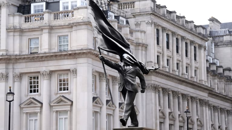 A statue of a man holding a flag which covers his face, left, and signed 'Banksy, has appeared in Waterloo Place in London.