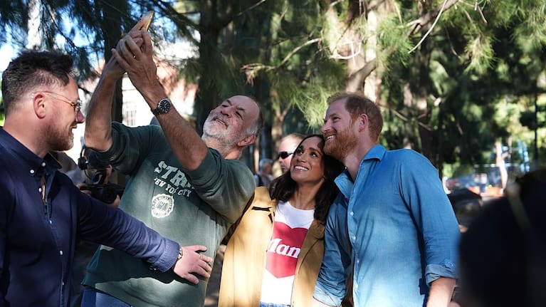 A team member for the Duke and Duchess of Sussex holds back a member of the public as they pose for a selfie photo at the Scar Tree Walk in Melbourne.