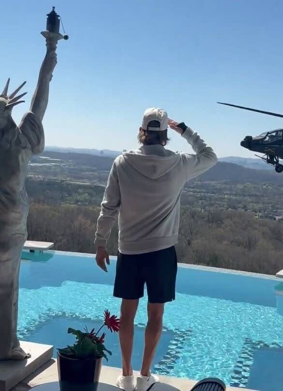 An individual dressed in a light-colored hoodie and cap stands on an elevated vantage point, gazing at the expansive landscape b