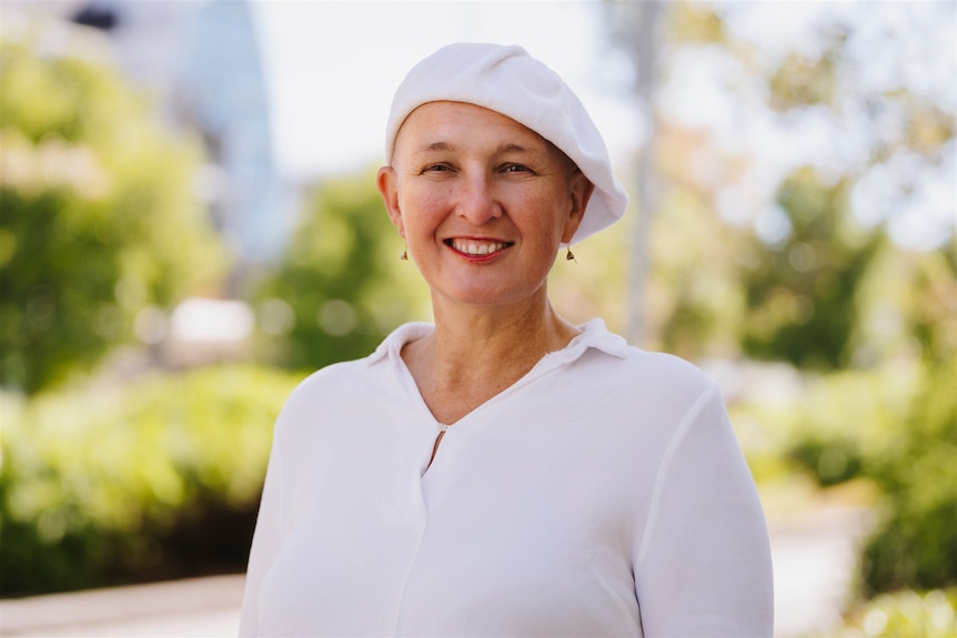 A woman with a white hat and a white shirt standing in an outside area in a park.
