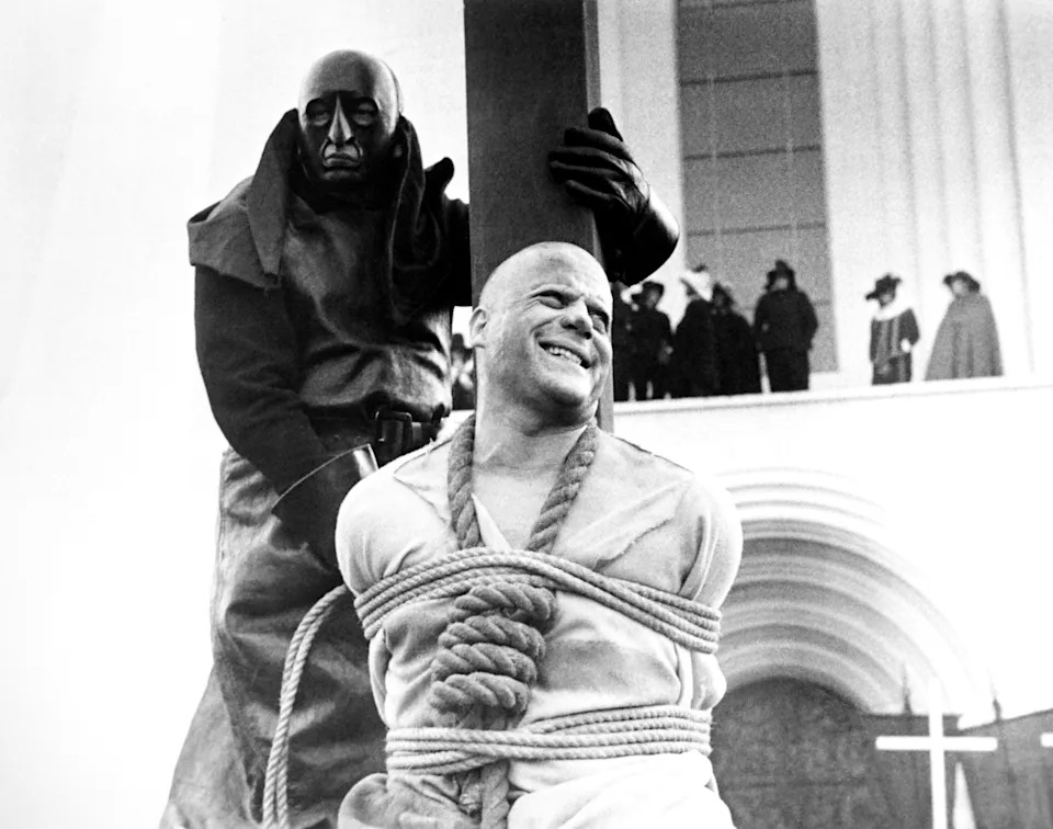 A person tied to a stake, with an executioner nearby, in a dramatic scene from an old film or historical reenactment