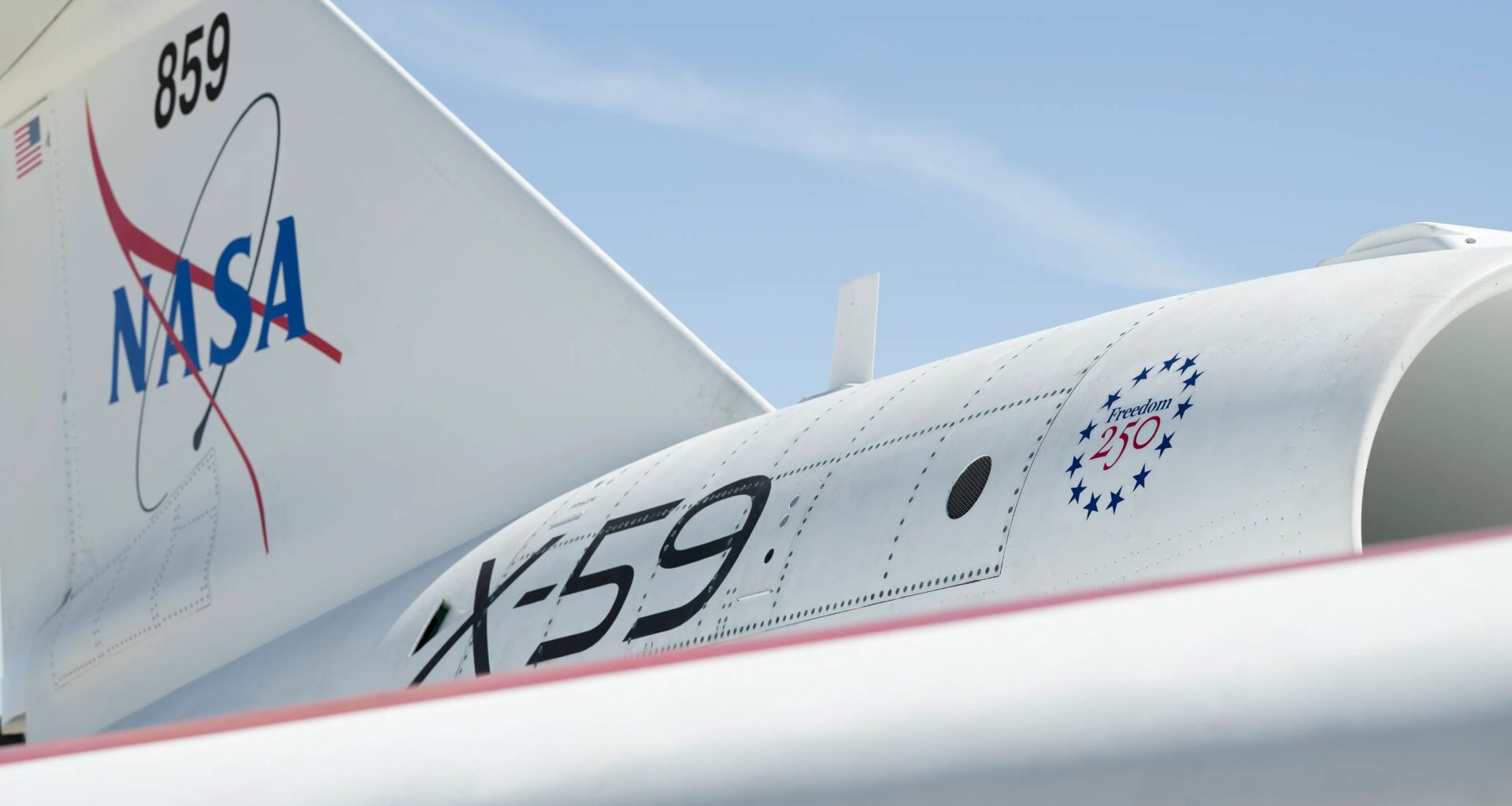 A close-up of NASA's X-59 tail showing a NASA graphic on the tail, X-59 on the side of the jet engine, and a Freedom 250 logo toward the front of the engine.