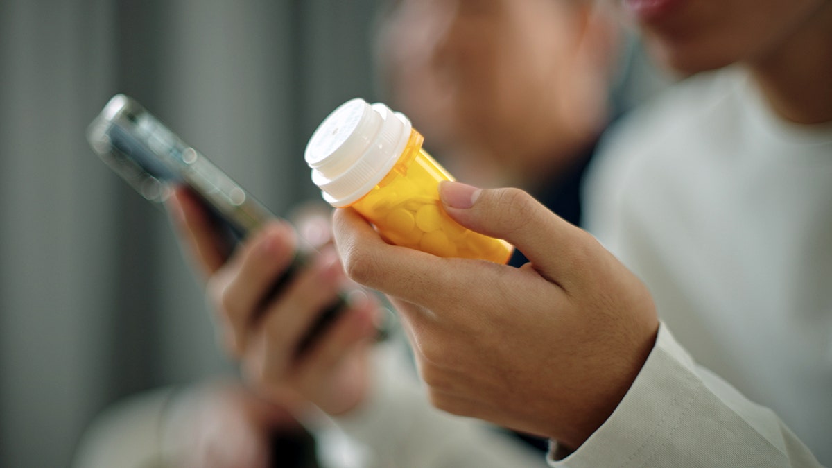 A person holds a prescription pill bpottle and a phone.