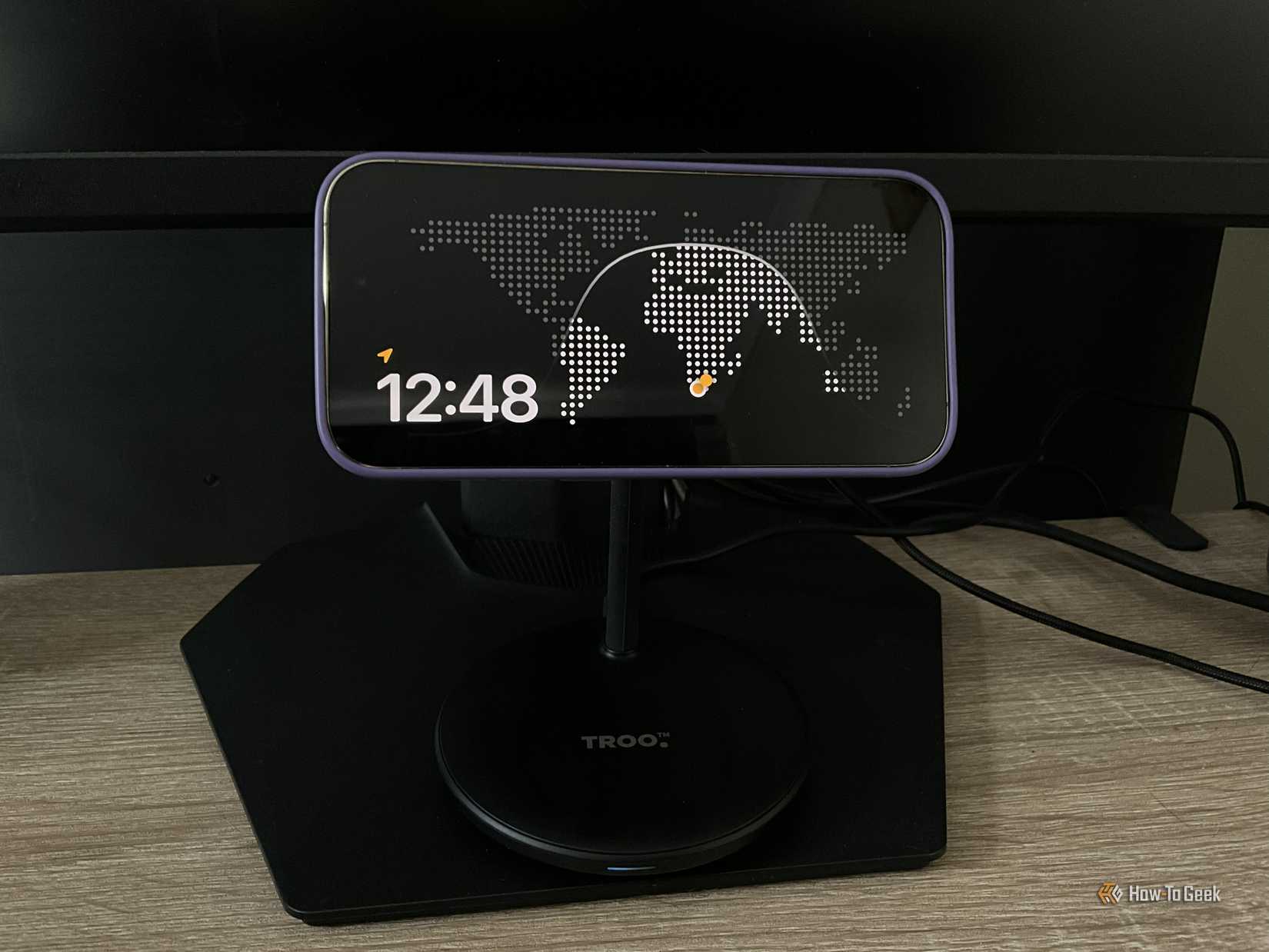 An iPhone showing a world clock sits no a desk.