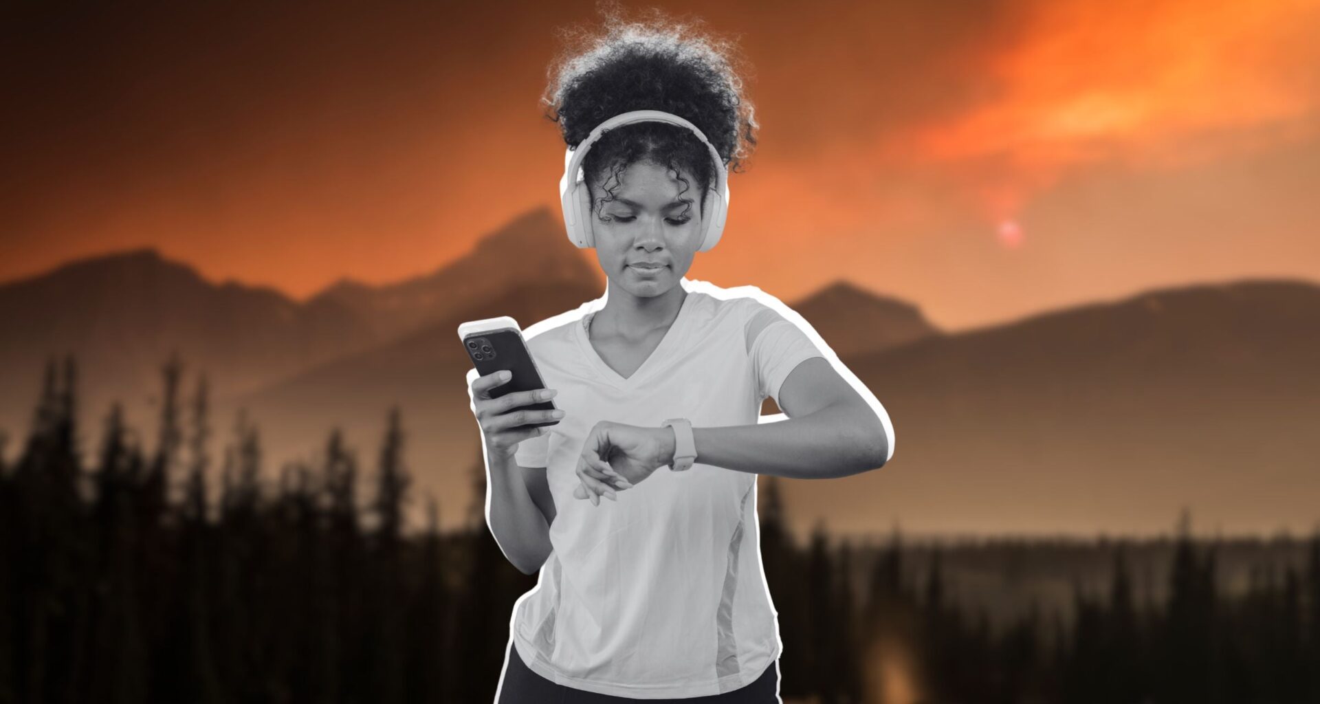 a woman holding her phone and checking her fitness watch. She has headphones over her ears.