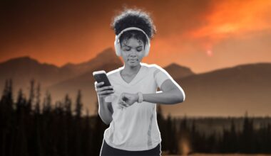 a woman holding her phone and checking her fitness watch. She has headphones over her ears.