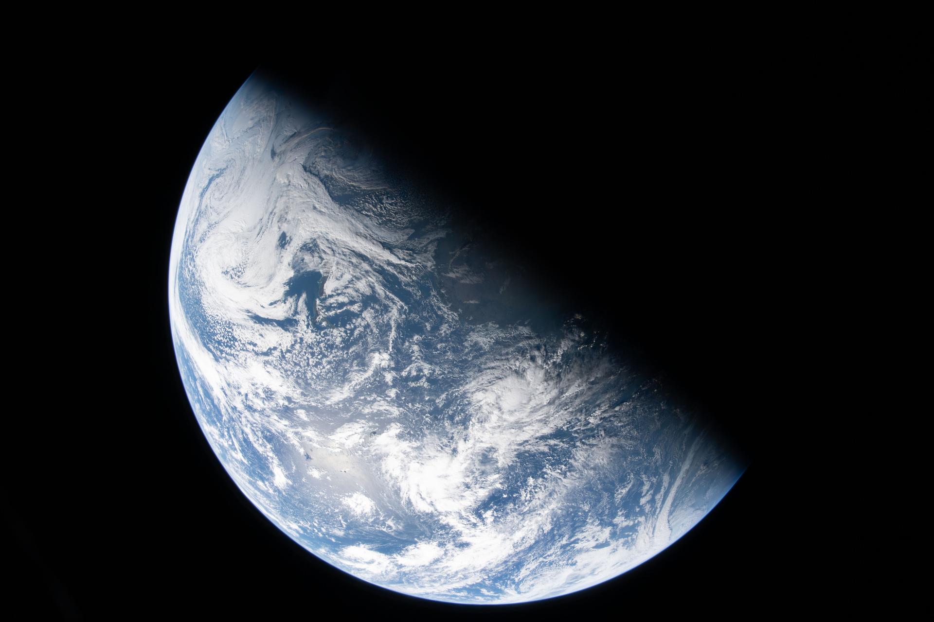 A view of Earth from space, partially illuminated, shows blue oceans, white clouds, and a shadow covering part of the planet—a perspective reminiscent of Artemis II’s journey and the hope it inspires for our moon and Earth.
