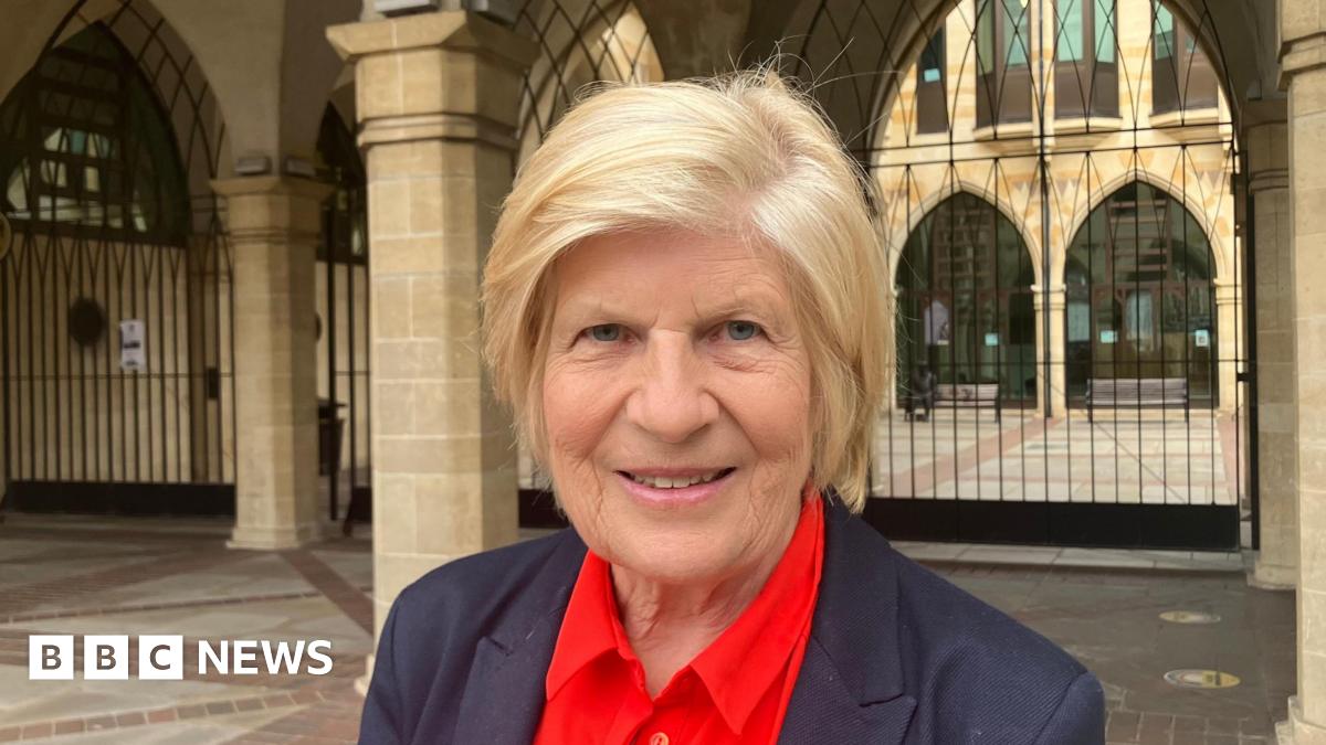 Sally Keeble is wearing a dark suit and red shirt. She has short blonde hair.