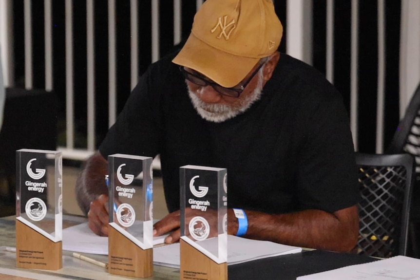 man wearing cap sits at table signing documents