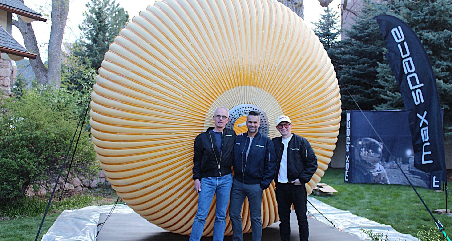 three people in jeans and blazers stand in front of a round crenellated structure in a field