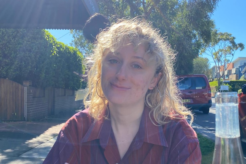 young woman with curly blonde hair smiles at the camera.
