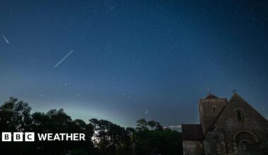 A tranquil nightscape capturing the starlit sky above an old English church graveyard. The silhouettes of weathered gravestones and the gothic architecture of the church create a serene yet mysterious foreground beneath a clear, star-filled sky. A peaceful fusion of history and the cosmos.